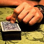 Deck of cards on table with hand holding top card.